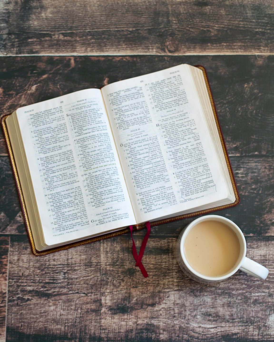 Otwarta Biblia ze wstążką jako zakładką leży na drewnianym stole obok kubka z kawą.