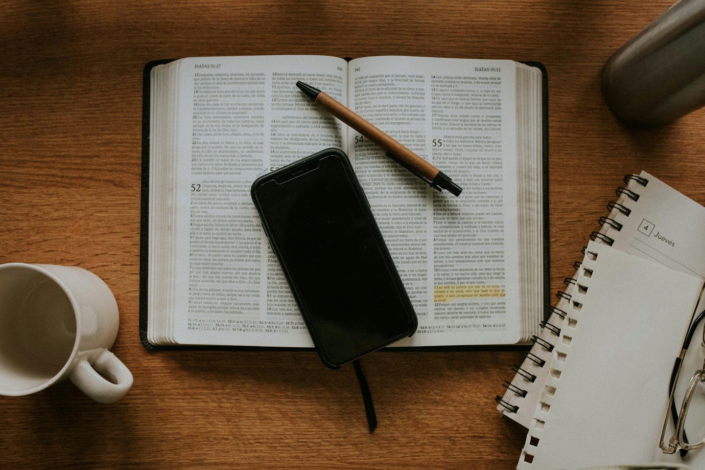 Otwarta Biblia ze smartfonem i długopisem na drewnianym biurku.