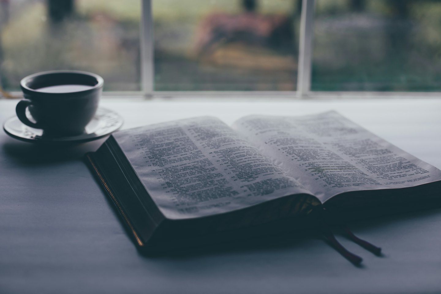 Otwarta Biblia i filiżanka kawy na parapecie.